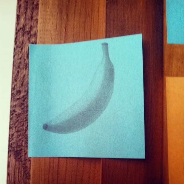 A blue Post-it note stuck to a wooden door, with a grayscale banana printed on it